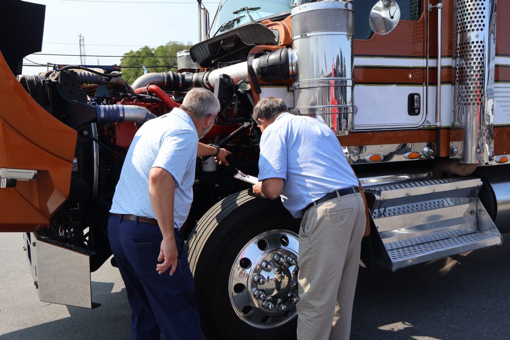 Two men inspecting under the hood of a Kenworth semi truck.