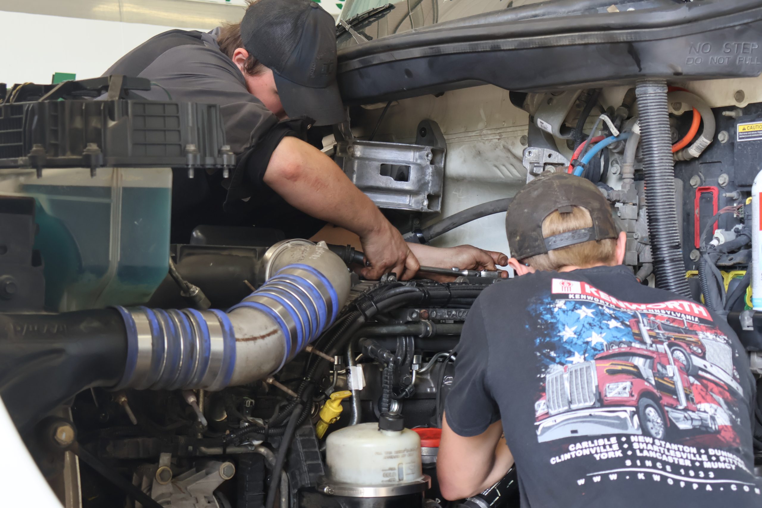 Two technicians working under the hood of a semi-truck
