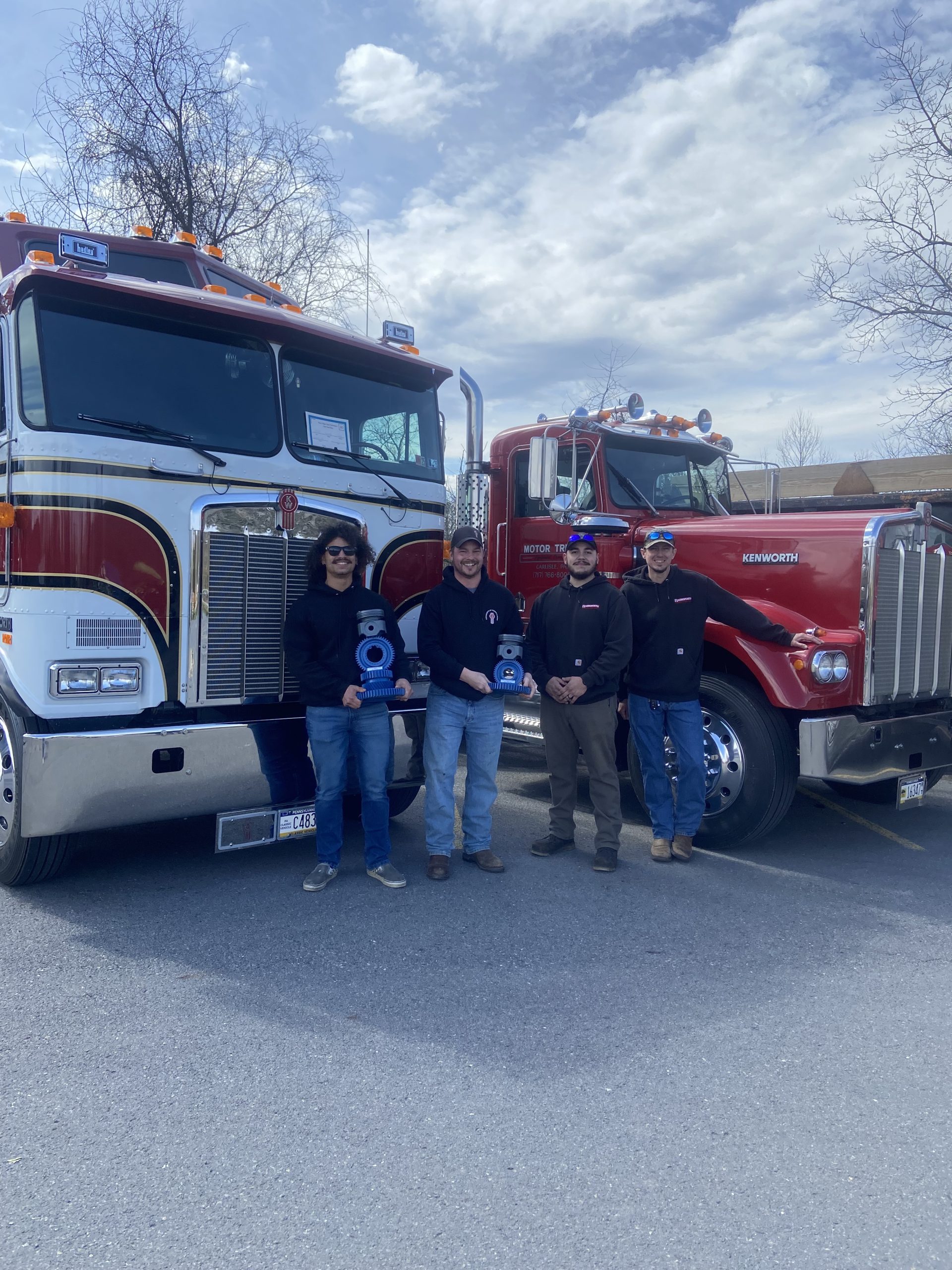 Four Men Standing In Front of Two Large Trucks Holding Awards